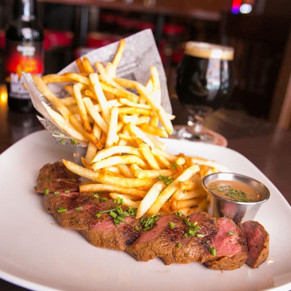 Sliced steak with fries, gravy, and a dark beer on a white plate at Firebird Tavern.