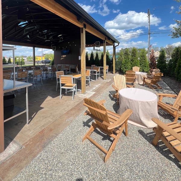Firebird Tavern's outdoor patio with covered seating, Adirondack chairs, and gravel ground under a sunny sky.