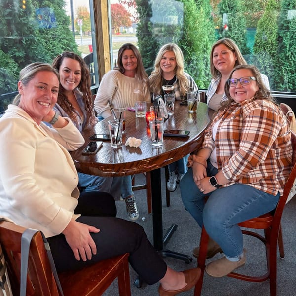 Six smiling women gathered around a wooden table with drinks at Firebird Tavern.