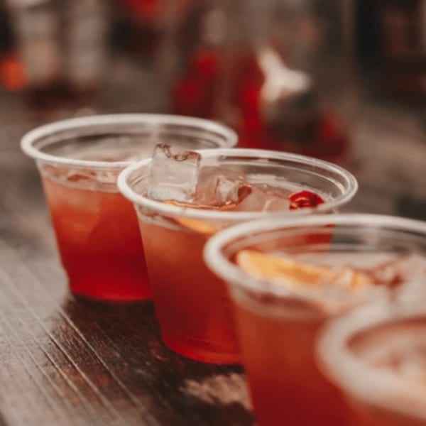 Row of Firebird Tavern cocktails in plastic cups with ice and orange slices on a wooden surface.
