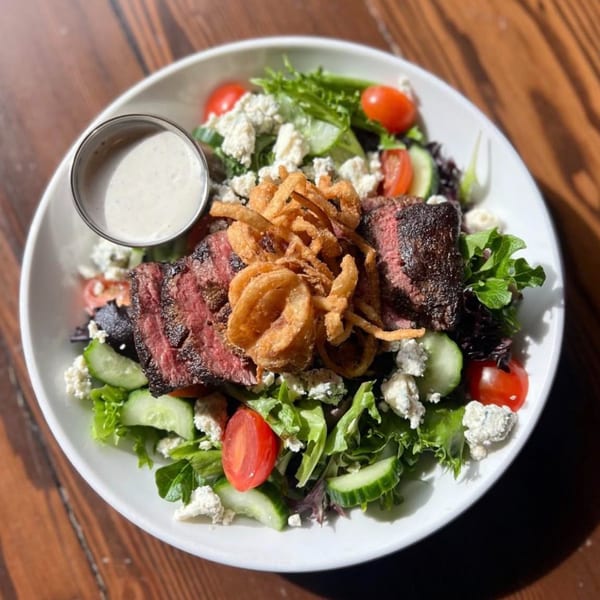 Firebird Tavern's steak salad with mixed greens, tomatoes, cucumbers, blue cheese, crispy onions, and dressing.