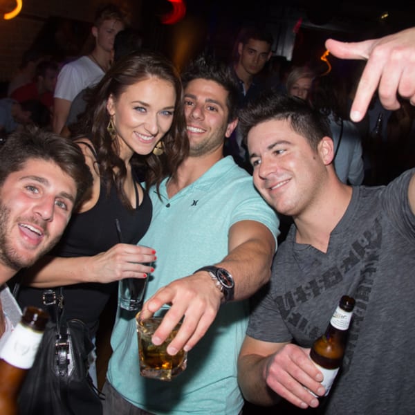 Four smiling young adults holding drinks and posing for a photo at Firebird Tavern.
