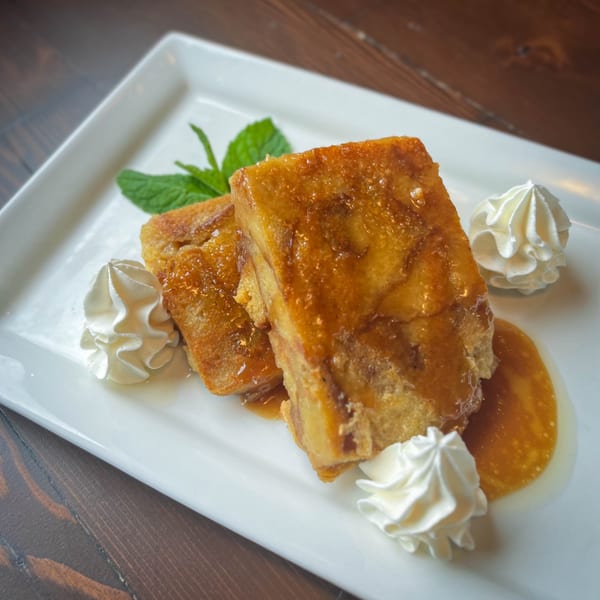 Two pieces of Firebird Tavern's French toast, drizzled with syrup, whipped cream, and mint on a white plate.