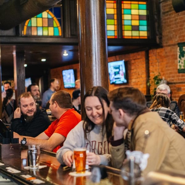 Patrons enjoying drinks and conversation at the Firebird Tavern bar, with stained glass windows in the background.