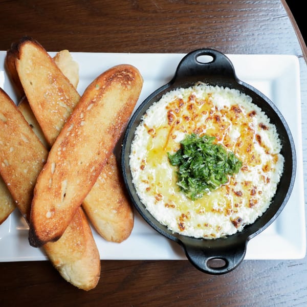 Firebird Tavern's baked cheese dip in a cast iron skillet with toasted bread slices on a white plate.