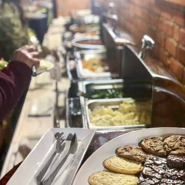 A person serves themselves from a buffet line with various hot dishes and desserts.