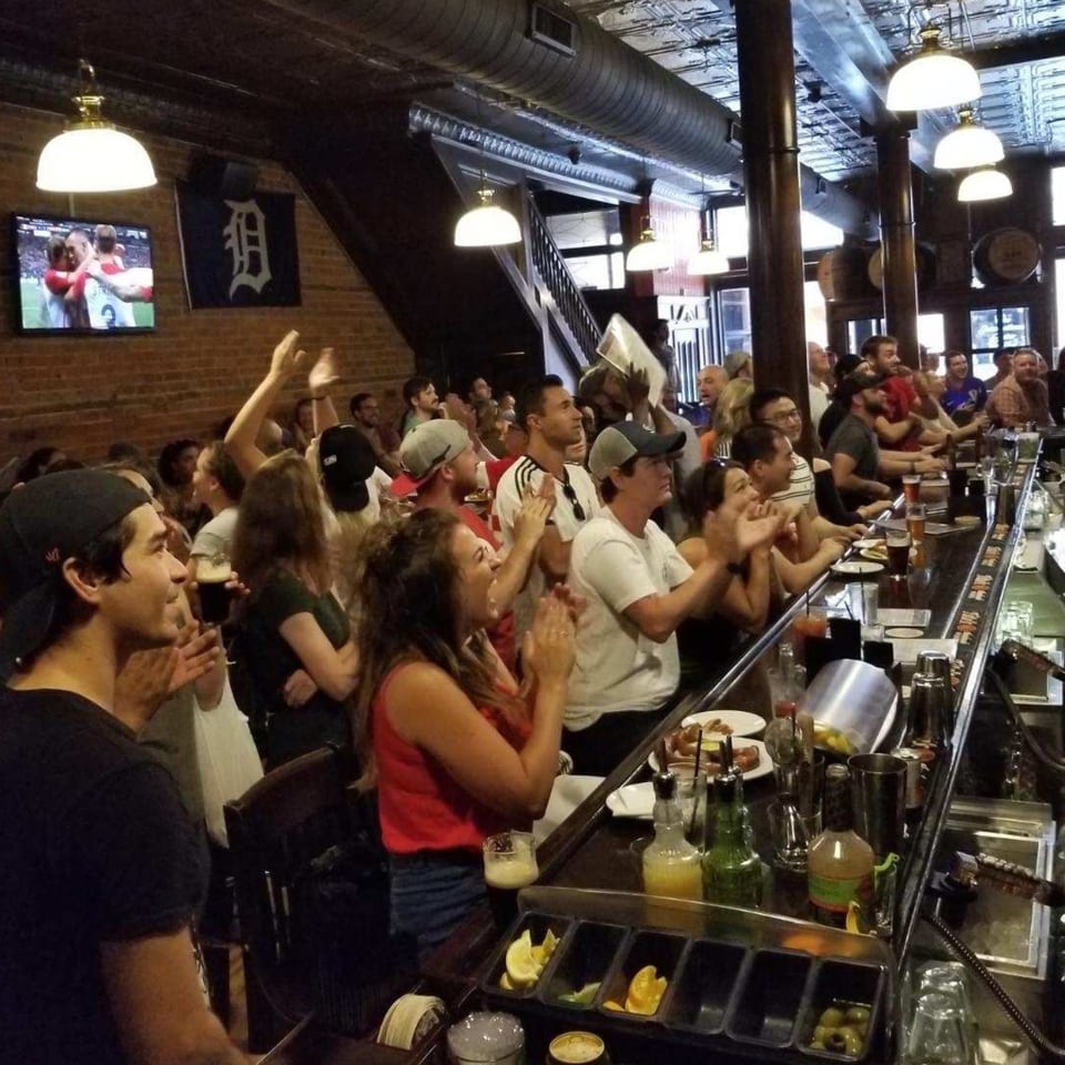 Patrons at Firebird Tavern bar watch a sports game on TV, clapping and cheering.