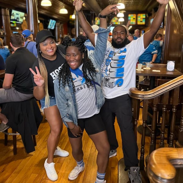 Three smiling people in sports attire pose inside Firebird Tavern, a lively bar-and-grill.