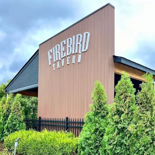 The Firebird Tavern building exterior with a brown facade, black roof, and green landscaping.