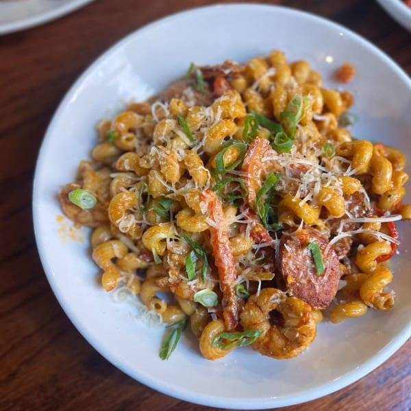 Firebird Tavern's Cajun Mac and Cheese with pasta, shrimp, sausage, and green onions in a white bowl.