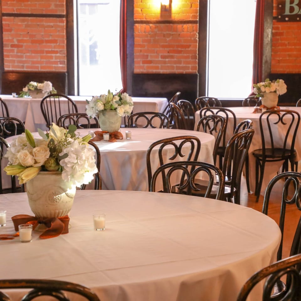 Elegant dining room at Firebird Tavern with round tables, white tablecloths, and floral centerpieces.