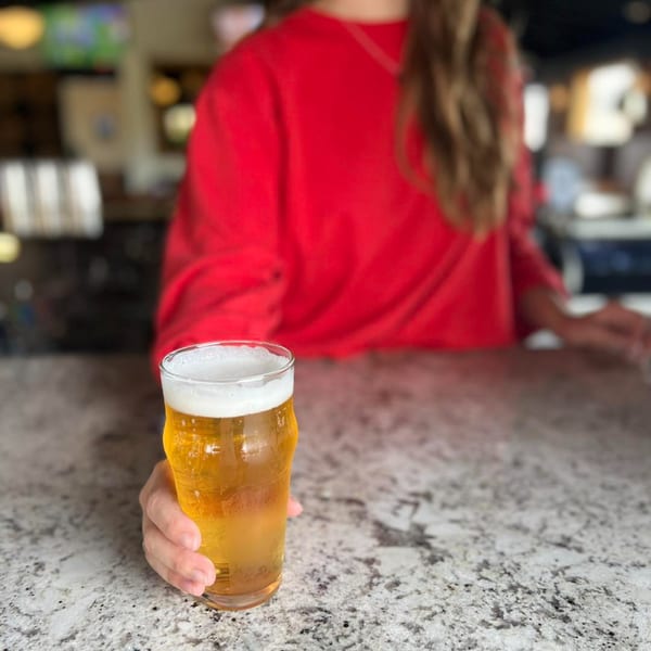 A person in a red shirt holding a glass of Firebird Tavern beer on a speckled bar counter.