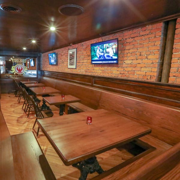 Interior of Firebird Tavern, showing a long row of wooden tables and booth seating against a brick wall.