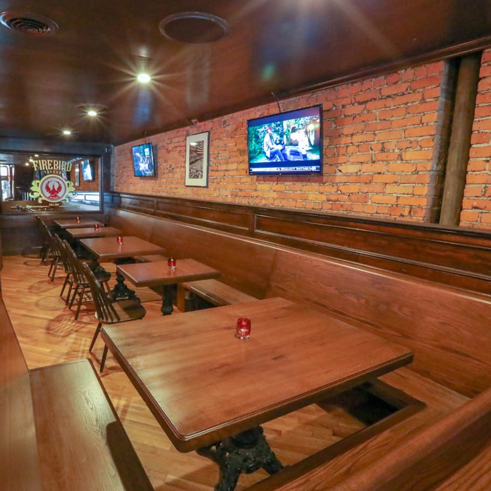 Interior of Firebird Tavern, showing a long row of wooden tables and booth seating against a brick wall.