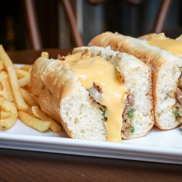 Cheesesteak sandwiches with melted cheese and a side of french fries on a white plate.