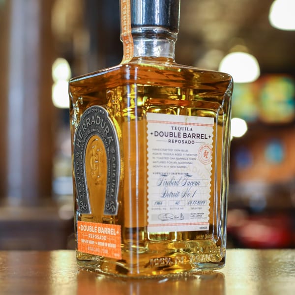 A bottle of Herradura Double Barrel Reposado Tequila, specially crafted for Firebird Tavern, on a wooden surface.