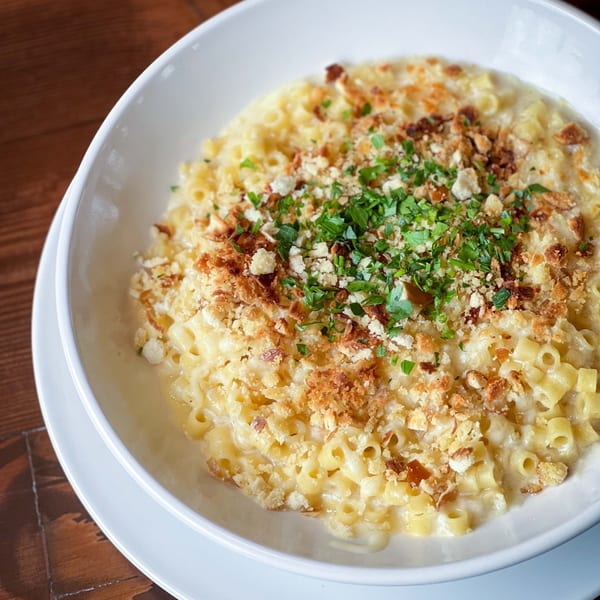 A white bowl of creamy macaroni and cheese topped with breadcrumbs and fresh parsley.