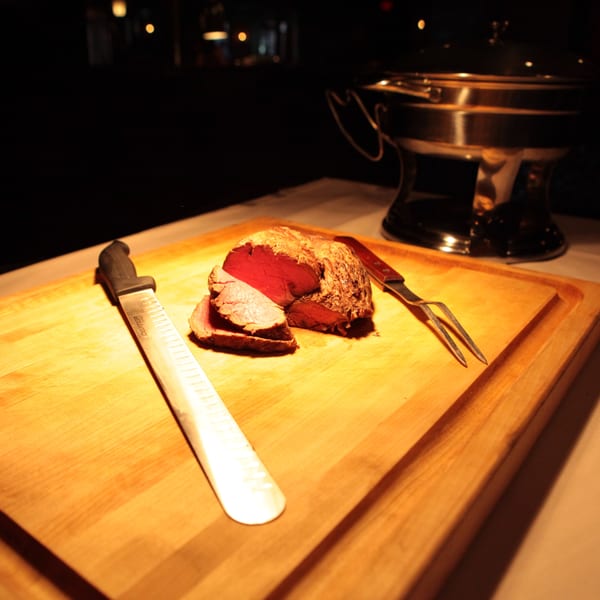 Carved roast beef with a carving knife and fork on a wooden board at Firebird Tavern.