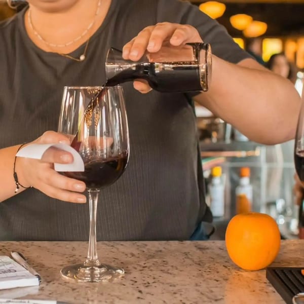A bartender pours red wine into a glass at Firebird Tavern, with an orange on the counter.