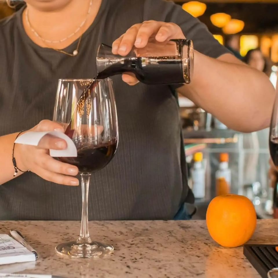 A bartender pours red wine into a glass at Firebird Tavern, with an orange on the counter.