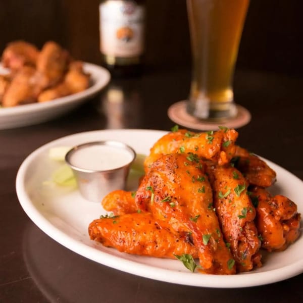 Firebird Tavern's buffalo wings with ranch dressing and celery, with a beer in the background.