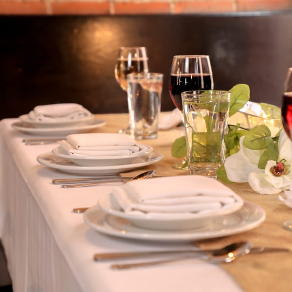 A set table at Firebird Tavern with white plates, folded napkins, and glasses of water and red wine.