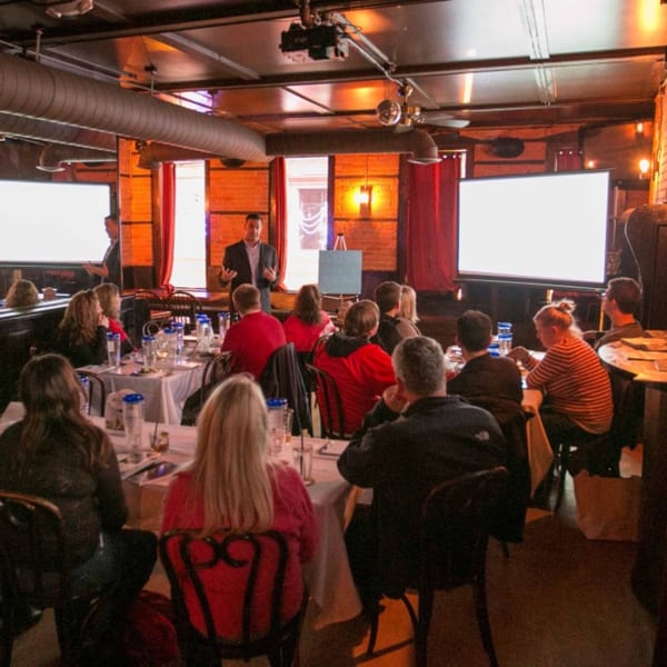 A speaker presents to an audience seated at tables in the Firebird Tavern dining room.