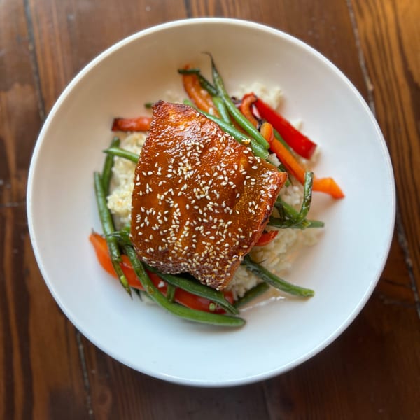 Firebird Tavern's sesame-crusted salmon with green beans, red peppers, and rice in a white bowl.