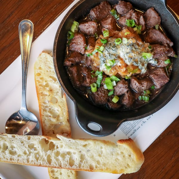 Firebird Tavern's beef bourguignon in a cast iron skillet with baguette slices and a spoon.
