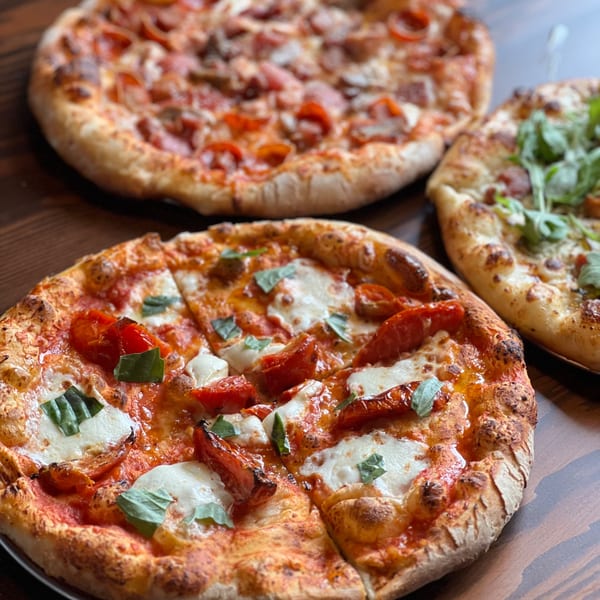 Three delicious pizzas, including a Margherita and a meat pizza, on a wooden table at Firebird Tavern.