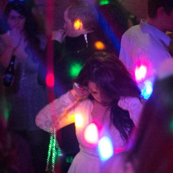 People dancing at Firebird Tavern, illuminated by colorful, blurry disco lights.